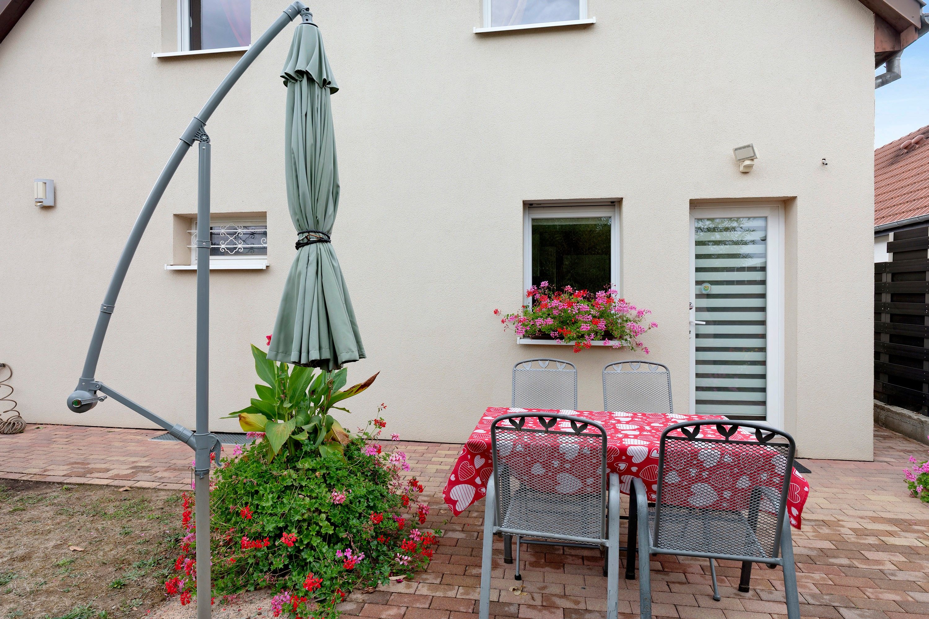 An outdoor patio with a table and chairs, a green umbrella, and potted plants.