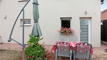 An outdoor patio with a table and chairs, a green umbrella, and potted plants.