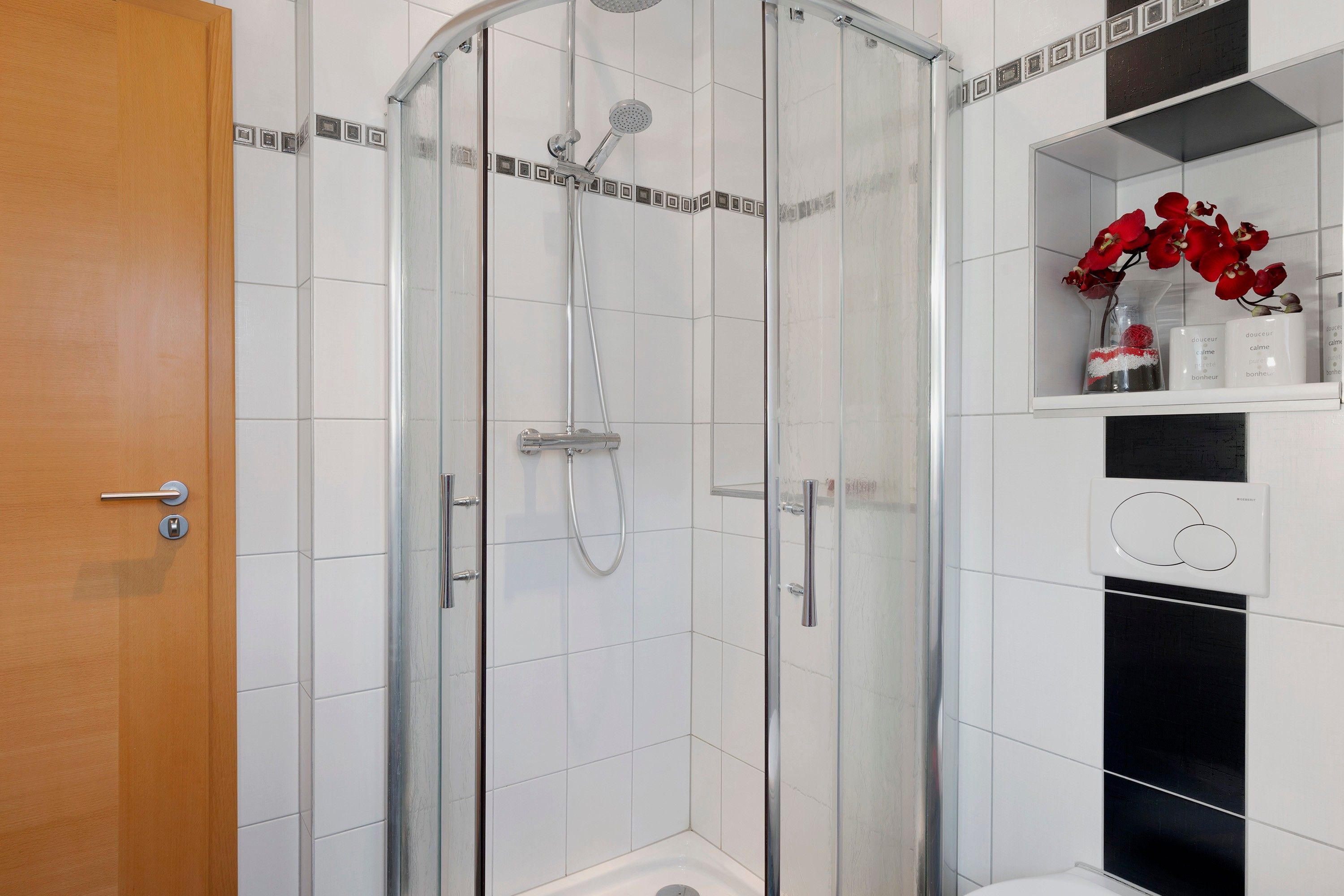 Une salle de bain moderne avec une douche à parois de verre, des carreaux blancs et une porte en bois.