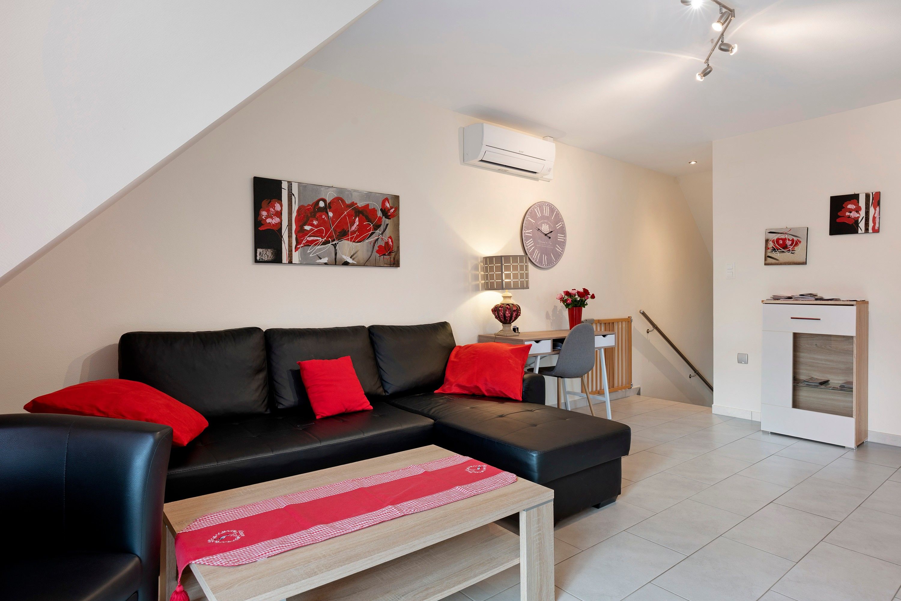 A modern living room with a black leather sofa, red cushions, a wooden coffee table, and a dining area with a chair and table.