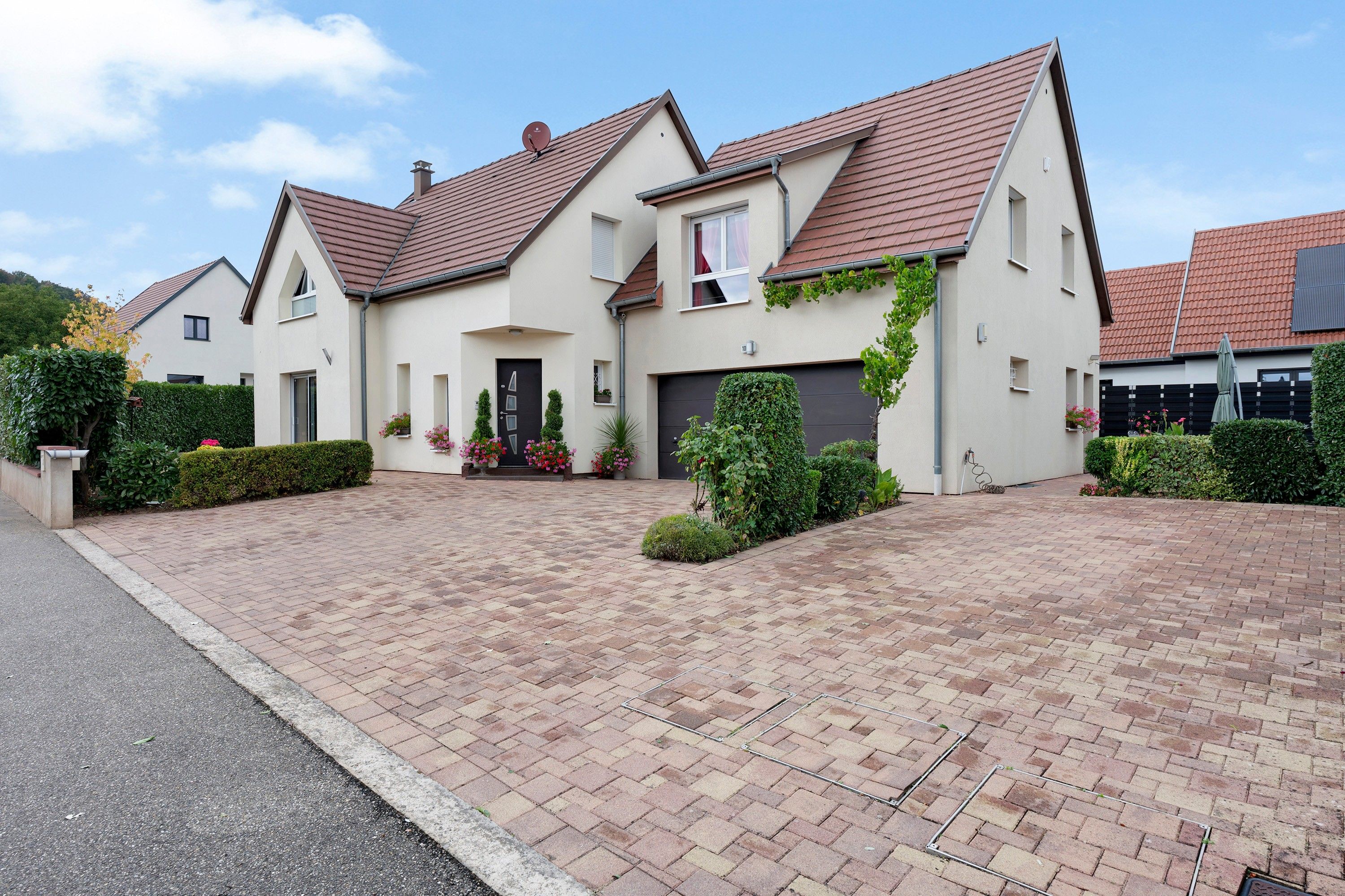 Une maison à deux étages avec une allée pavée, un garage et un jardin bien entretenu.