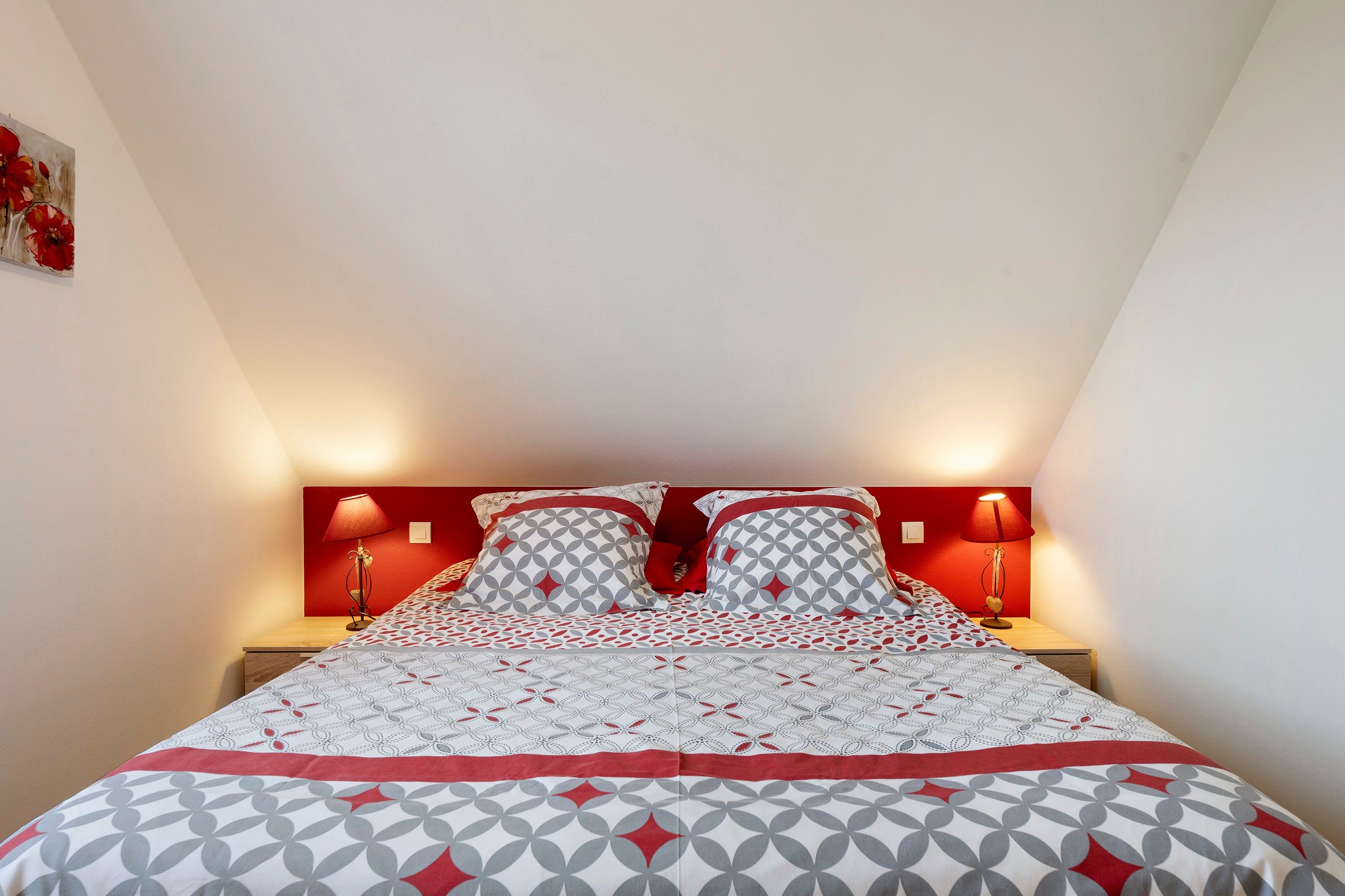 A bed with a geometric patterned bedspread, two pillows with a circular design, and two bedside lamps on a wooden nightstand.