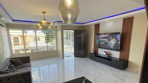 Una sala moderna con piso de mármol, un sofá, un televisor y una lámpara colgante original.