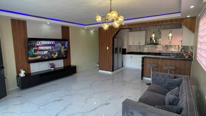 Una sala de estar moderna con un televisor de pantalla plana, un sofá gris y una cocina con salpicadero de mármol.