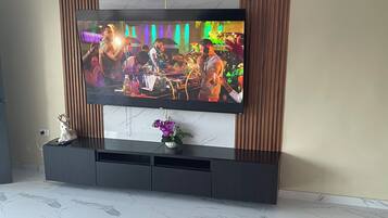 A flat-screen TV mounted on a wall with a wooden panel design, a marble-tiled floor, and a small decorative plant on the entertainment unit.