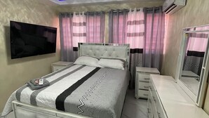 Un dormitorio con cama, mesitas de noche, cómoda, televisor y cortinas.