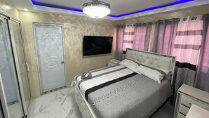 Un dormitorio con cama, mesitas de noche, televisor y lámpara en el techo.