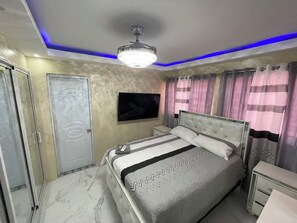 A bedroom with a bed, bedside tables, a television, and a ceiling light fixture. - Comfort One-Bedroom Apartment (Santo Domingo)