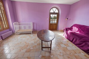 Ein Zimmer mit einem Babybett, einem runden Tisch und einem violetten Sofa.