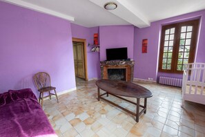 A room with purple walls, a fireplace, a television, and a window with a view. - Gite La Tour D - Chateau Grange Arthuis with Shared Garden, Wi-Fi, and Air Conditioning (Lavau)