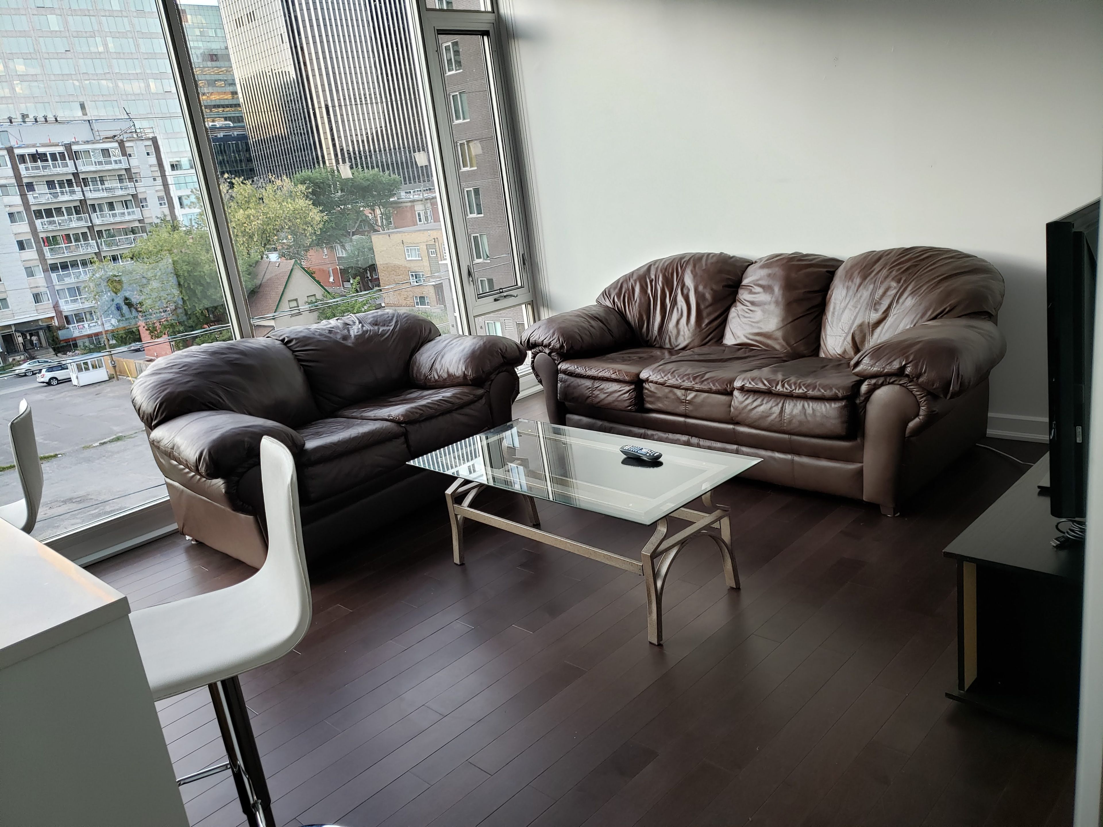 Un salon moderne avec deux canapés en cuir, une table basse en verre et une vue sur le paysage urbain grâce à de grandes fenêtres.
