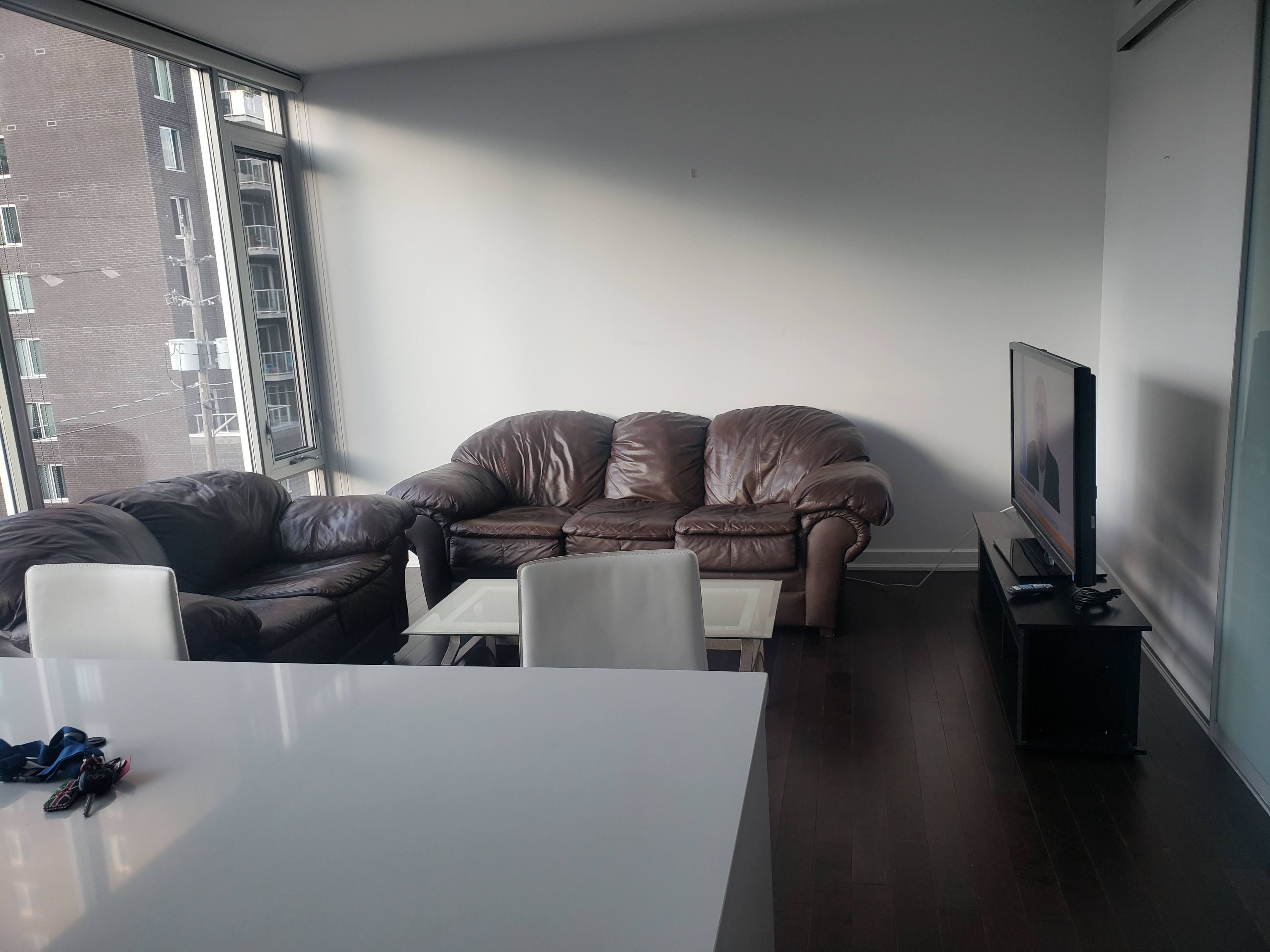 A modern living room with a brown leather sofa, a white coffee table, and a television on a stand.