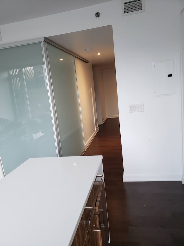 A modern hotel room with a large sliding glass door, a wooden floor, and a white wall with a light switch.