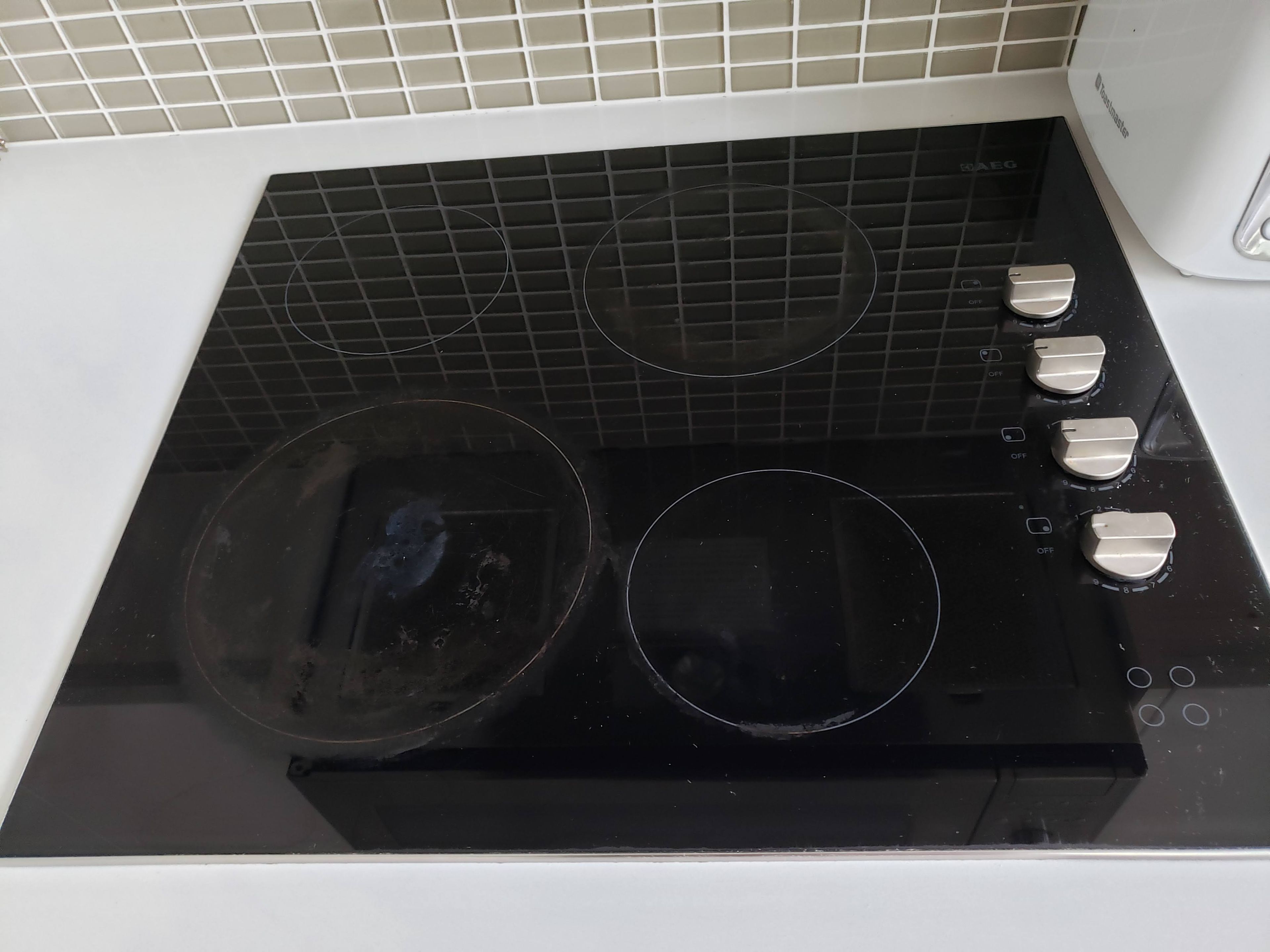 Une cuisine avec une plaque de cuisson noire, trois brûleurs et un mur blanc agrémenté d’un pare-feu en carreaux.