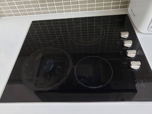A kitchen with a black stovetop, three burners, and a white wall with a tiled backsplash.