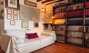 Un saló tranquil amb un sofà blanc, un coixí vermell, quadres emmarcats, un mapa i una prestatgeria plena de llibres.