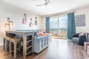 A spacious living area with a grey sofa, a wooden dining table with chairs, and a balcony with a view of the city skyline. - The Fern & Fiddle by Stay Local Nashville - Skyline Views & Games Near Downtown (Nashville)