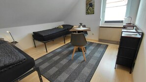 A compact room with a bed, a desk, a chair, a radiator, and a window.