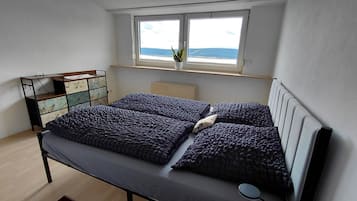 A bedroom with a bed, a dresser, a window with a plant, and a radiator.