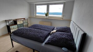 A bedroom with a bed, a dresser, a window with a plant, and a radiator.