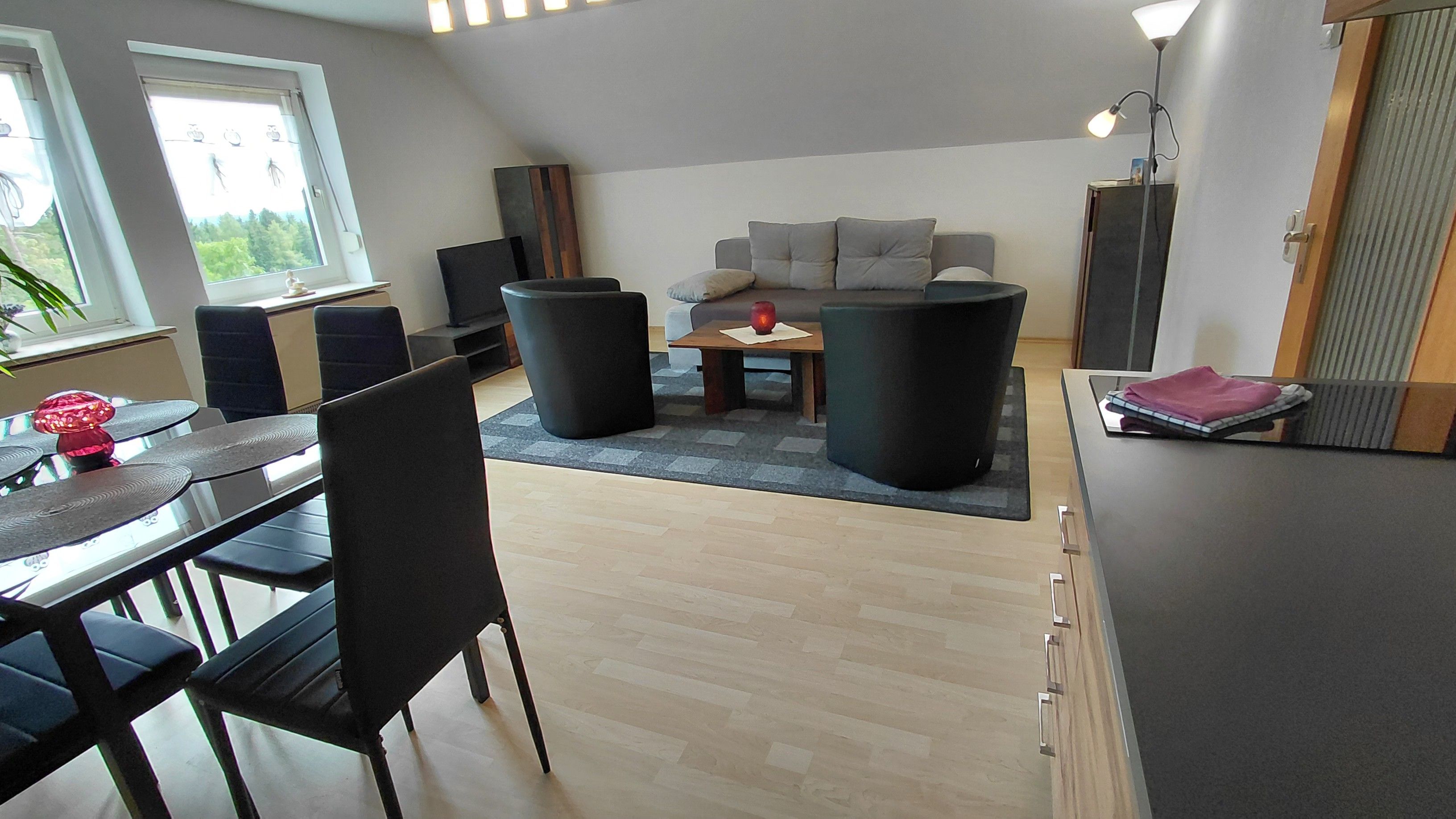 Ein modernes Wohnzimmer mit einer Couch, zwei schwarzen Sesseln, einem Couchtisch und einem Essbereich mit Tisch und Stühlen.
