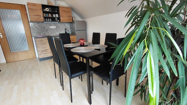 A dining area with a table set for four, surrounded by chairs, in a room with a kitchen in the background.
