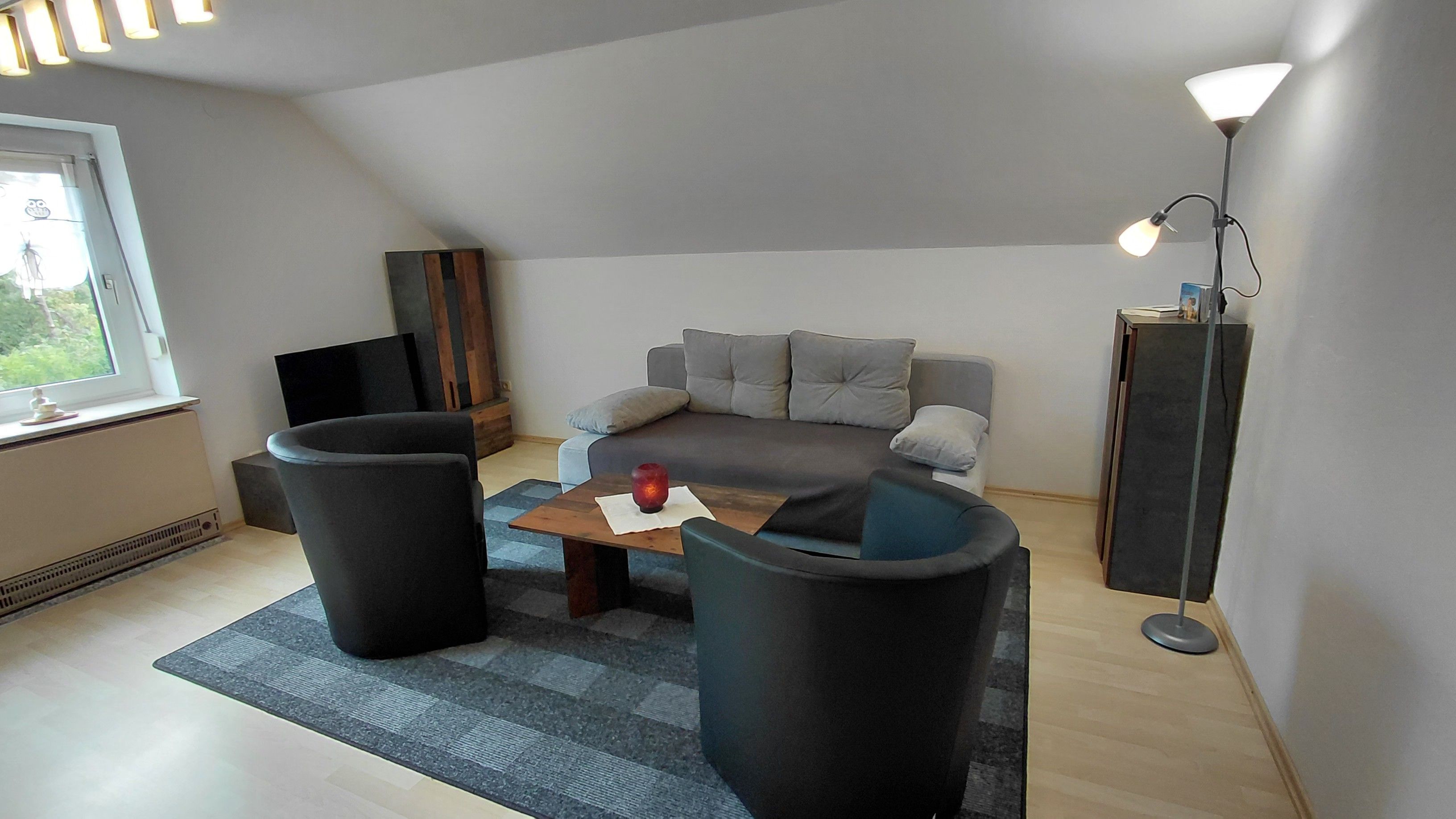 A modern living room with a grey sofa, two black armchairs, a wooden coffee table, and a floor lamp.