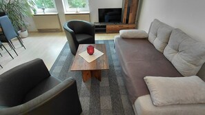 A living room with a sofa, armchair, and a coffee table with a candle. - Apartment Naturoase Fichtelberg Kira & Suki with Mountain View and Wi-Fi (Fichtelberg)