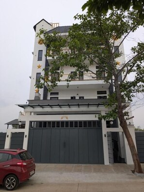 Ein mehrstöckiges Wohngebäude mit einer Garage, einem roten Auto davor und einem Baum zur Rechten.
