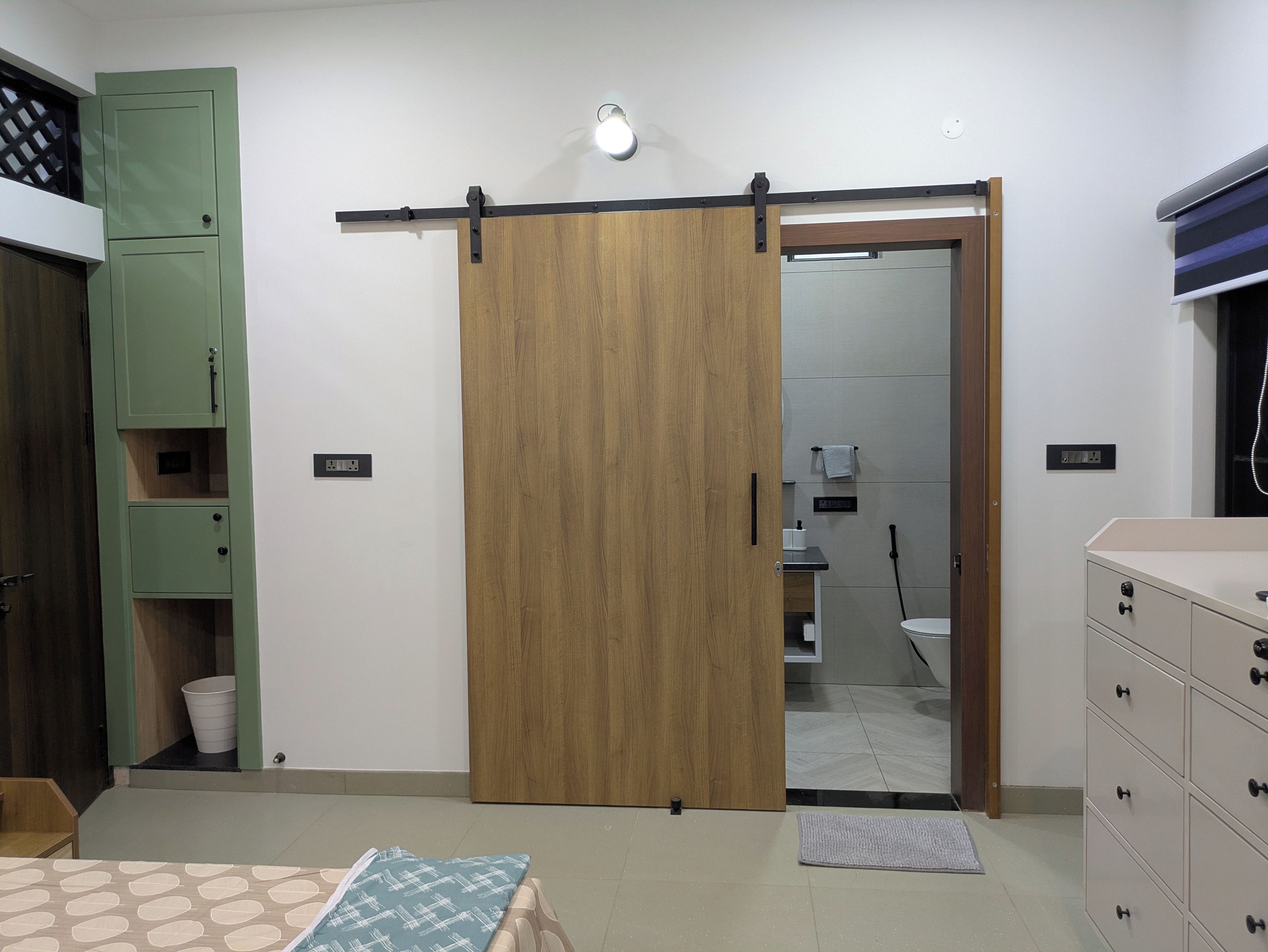 A room with a sliding wooden door, a green cabinet, a bed with patterned bedding, and a dresser with drawers.