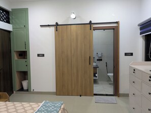 Ein Zimmer mit einer Schiebetür aus Holz, einem grünen Schrank, einem Bett mit gemusterten Betttextilien und einer Kommode mit Schubladen.
