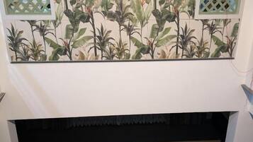 A dining area with a wooden table and chairs, a decorative wall with a botanical pattern, and a lattice window design.
