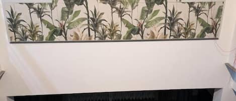 A dining area with a wooden table and chairs, a decorative wall with a botanical pattern, and a lattice window design.