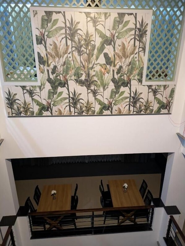 A dining area with a wooden table and chairs, a decorative wall with a botanical pattern, and a lattice window design.