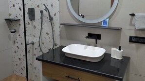 A bathroom with a shower, a sink, a mirror, and a towel rack. - Abhimaan (Mysore)