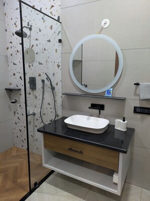 Un baño con ducha, lavamanos, espejo y toallero.