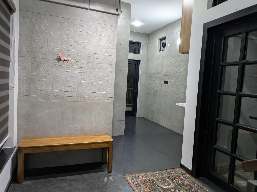 A hallway with a bench, a patterned wall, a door, and a rug.