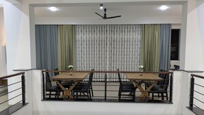A dining area with a table and chairs, a ceiling fan, and curtains. - Abhimaan (Mysore)