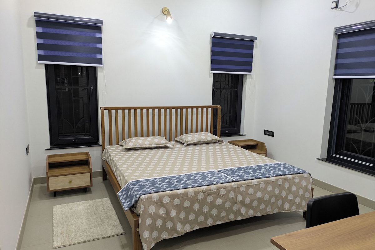 Un dormitorio con una cama individual, mesitas de noche, un escritorio y dos ventanas con persianas.