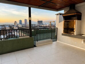A balcony with a view of a cityscape, a barbecue grill, and a tiled floor.