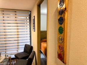 A hotel room with a bed, a chair, a window with blinds, and a wall with decorative metalwork.