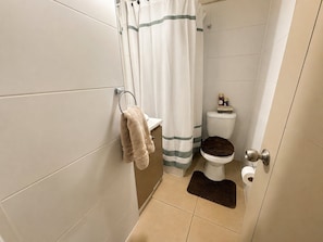 A bathroom with a toilet, a towel rack, a shower curtain, and a mat. - Oceana Suites Parque Bicentenario (cerrillos)