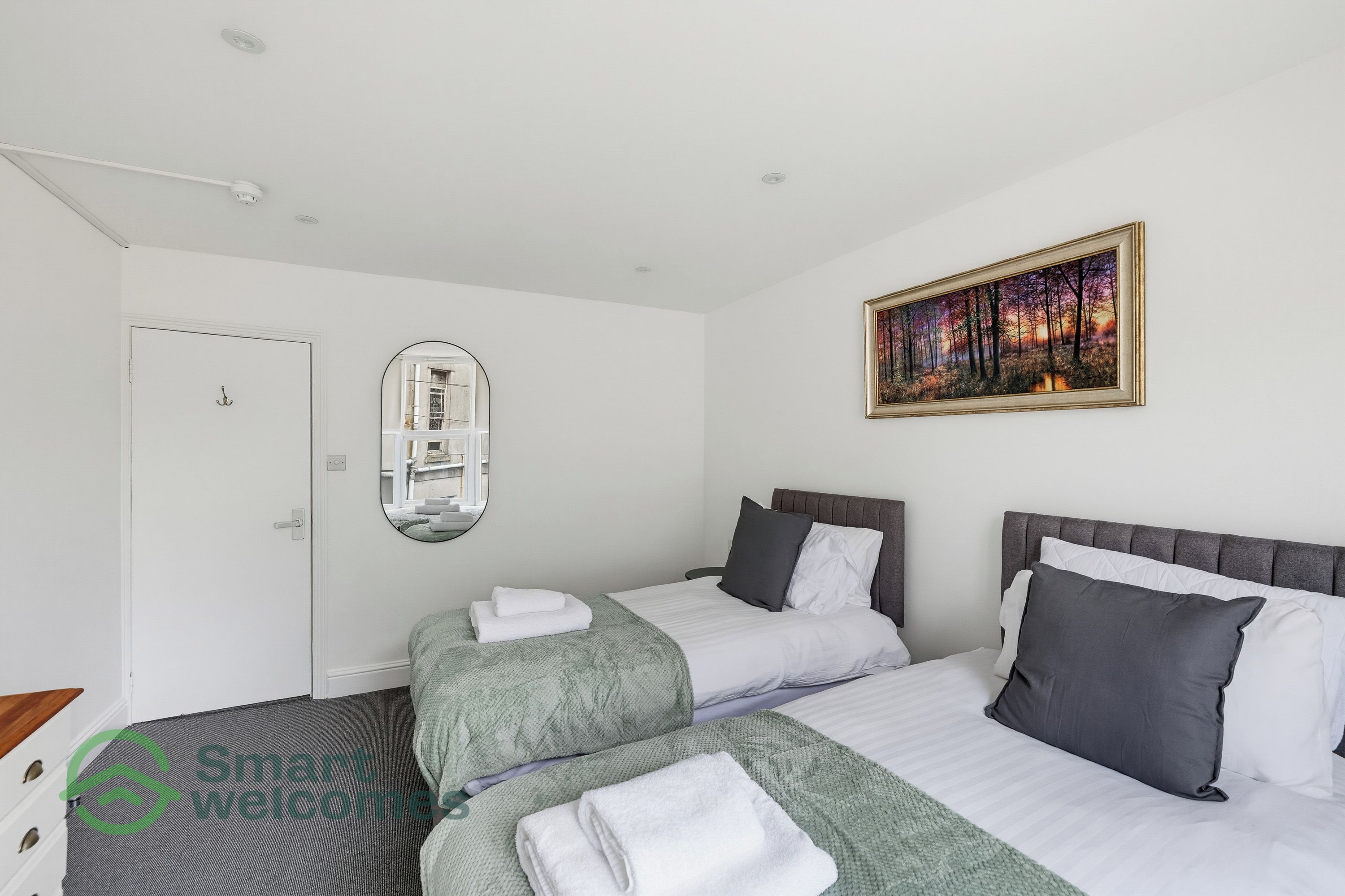 A hotel room with two beds, a painting, a mirror, and a door.