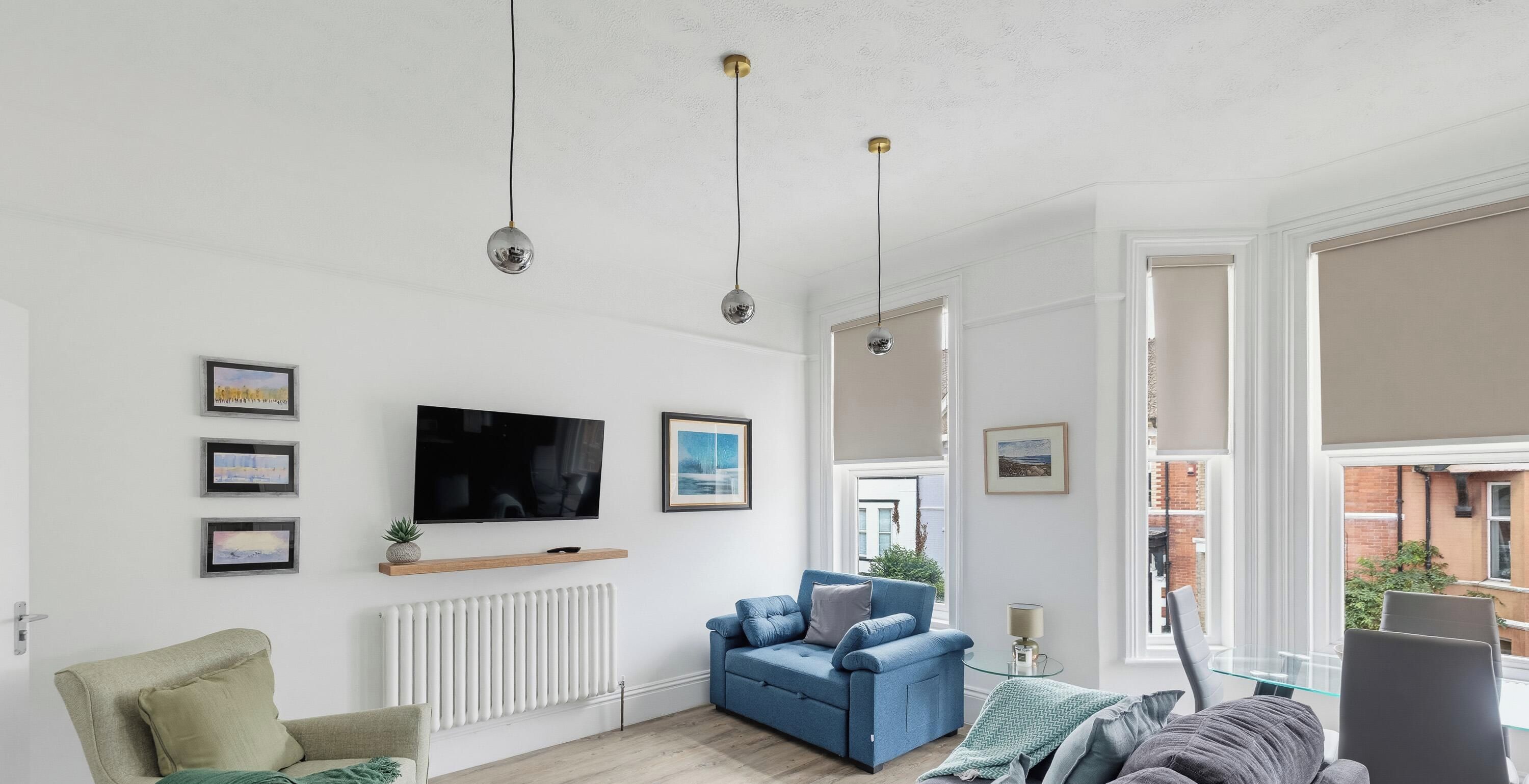 Un salon moderne avec un canapé bleu, un téléviseur et des tableaux encadrés accrochés au mur.