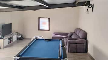 Een kamer met een pooltafel, een bank, een televisie en een raam.