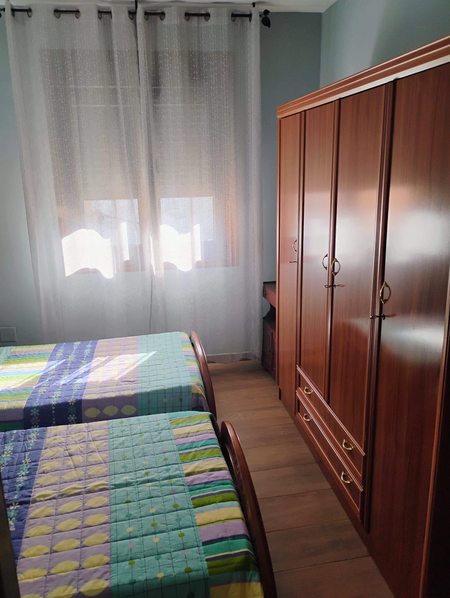 Een slaapkamer met twee bedden, een houten garderobe en een raam met dunne gordijnen.