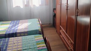 A bedroom with two beds, a wooden wardrobe, and a window with sheer curtains. - Holiday Home 'Beiramar' with Private Terrace and Wi-Fi (Boiro)