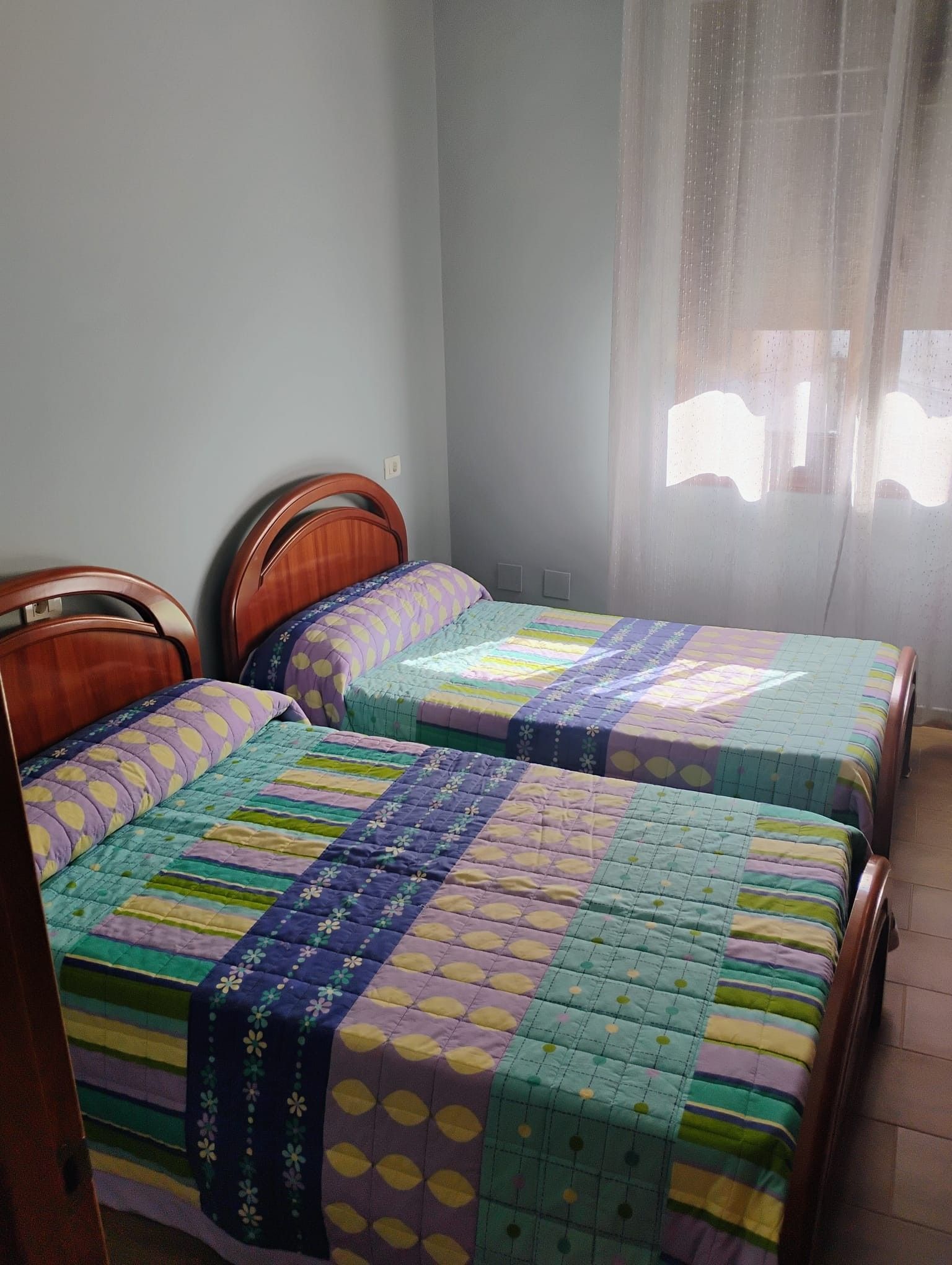 Une chambre avec deux lits en bois, chacun recouvert d’une couverture aux couleurs vives.