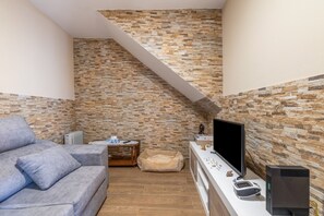 A living room with a stone wall, a grey sofa, a wooden coffee table, a flat-screen TV, and a small heater. - Holiday Home 'Beiramar' with Private Terrace and Wi-Fi (Boiro)