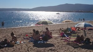 A beach with people sunbathing, umbrellas, and a clear view of the sea and distant mountains.